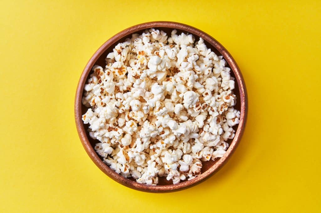 Bowl of salty popcorns on a yellow background