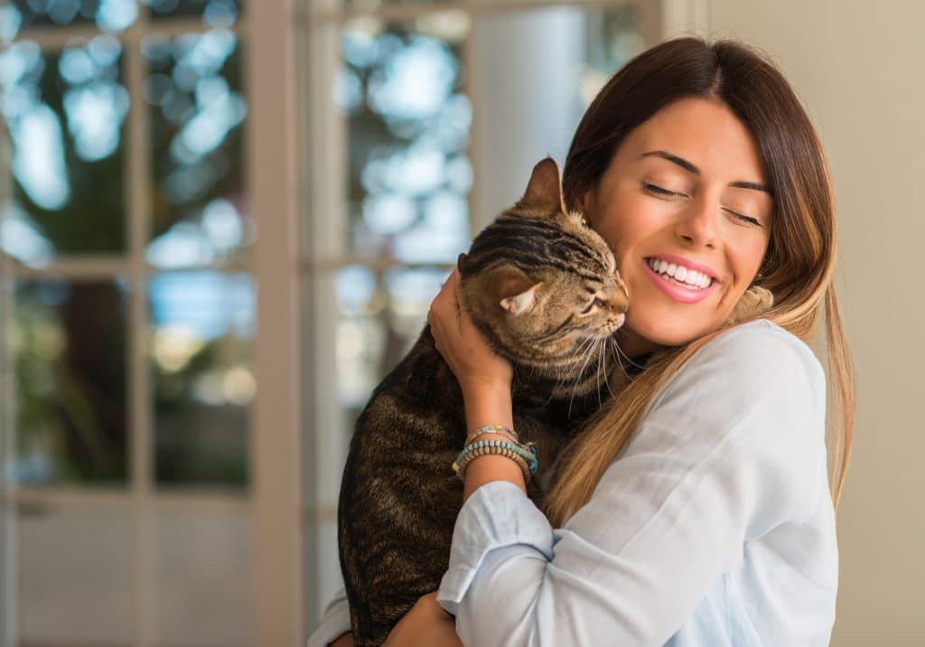 Young beautiful woman smiling and cuddling cat with love at home.